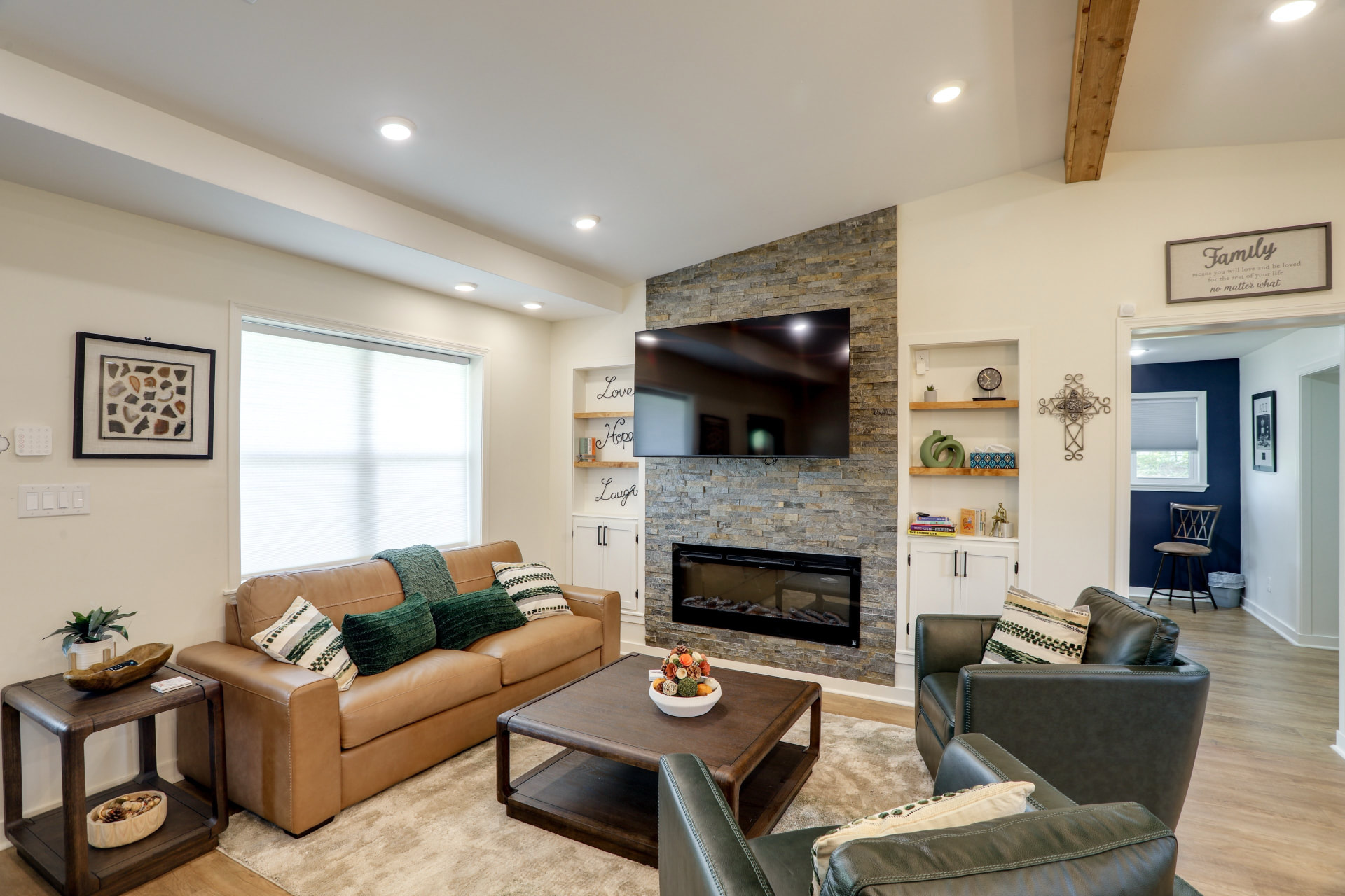 Living room at Cedarstone Retreat with a stacked-stone fireplace, mounted TV, leather sofa and swivel chairs