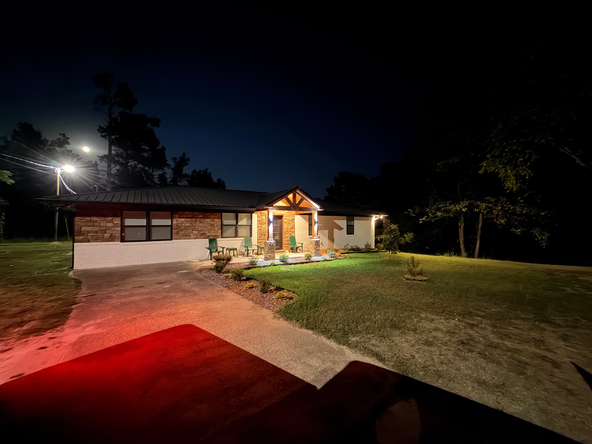 Angled evening view of Cedarstone Retreat showing the illuminated porch, driveway, lawn, and surrounding trees