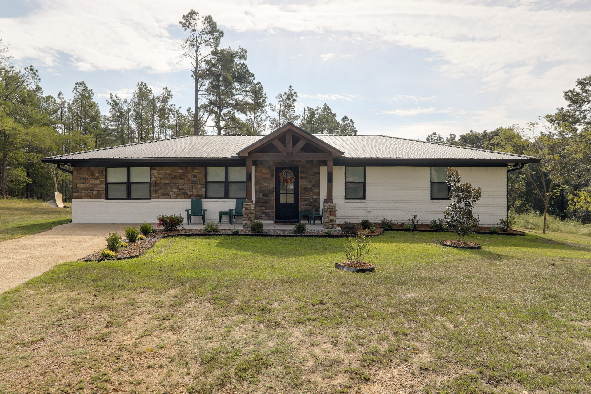 Straight-on daytime view of Cedarstone Retreat, a single-story stone and white-brick home with a covered front porch and landscaped lawn