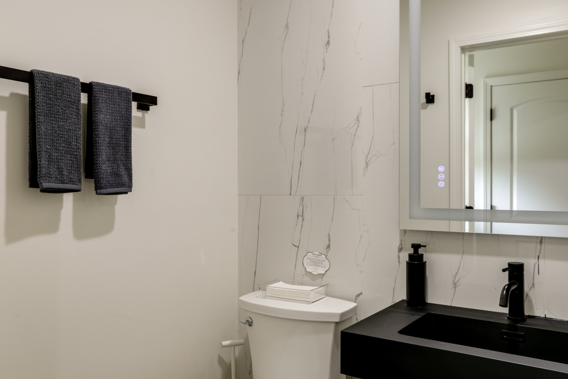 Bathroom vanity at Cedarstone Retreat with a black sink, marble-look tile, and lighted mirror