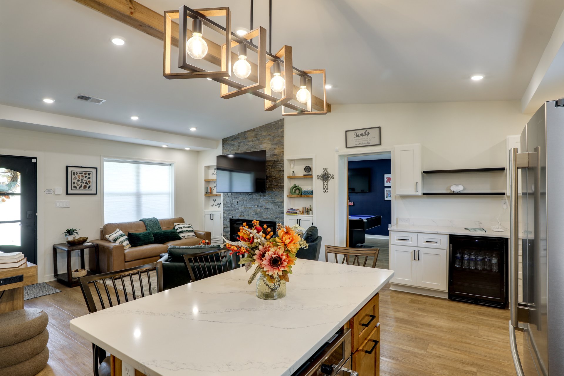 Wide view over the kitchen island at Cedarstone Retreat toward the living room's stone fireplace, with the coffee bar and the game room doorway beyond